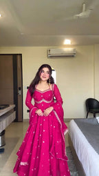 Woman in a pink traditional outfit standing in a room with an air conditioner on the wall.